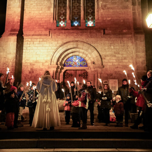 Groupe de personnes avec des flambeaux devant l'église pour l'animation balade contée