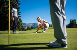 Three people playing golf with a woman putting the ball down.